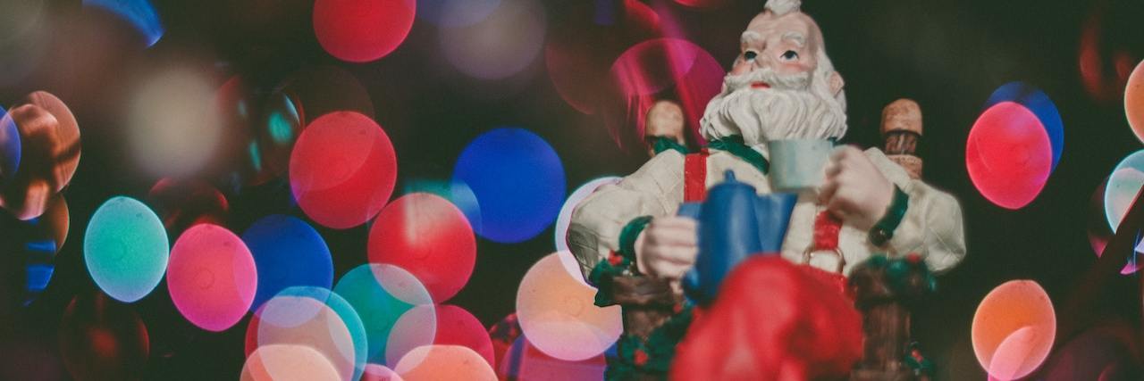 How to Practice Self-Care in a Pandemic: Holiday Edition A Santa sculpture with a cup of tea, sitting in lights