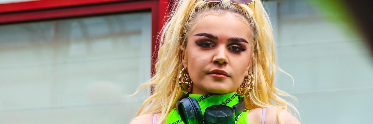 What Hypersexuality Feels Like During a Bipolar Manic Episode Woman with long blonde hair in a high ponytail leans against a railing wearing a neon green tank top and headphones around her neck