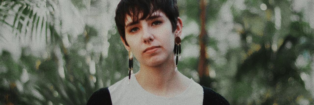 photo of person with short hair looking into camera with serious expression and plants behind them