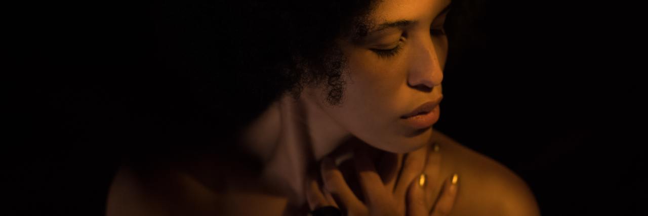 The Inability to Feel Pleasure Is Depression's Hardest Symptom photo of woman with her eyes closed and hands raised to her chest, looking away, against black background