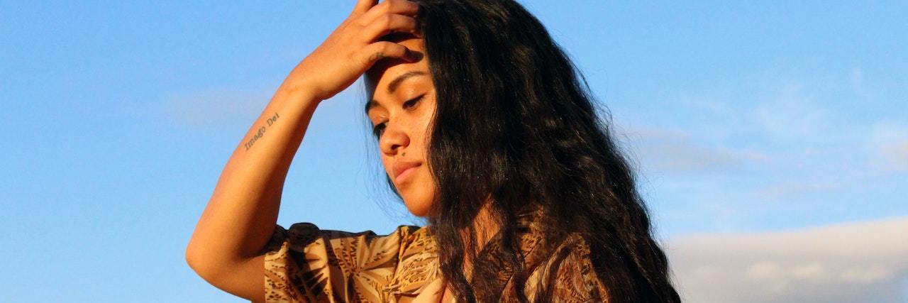 What Happens After You Survive a Suicide Attempt A woman standing outside. The sky is blue, and she's running her fingers through her hair