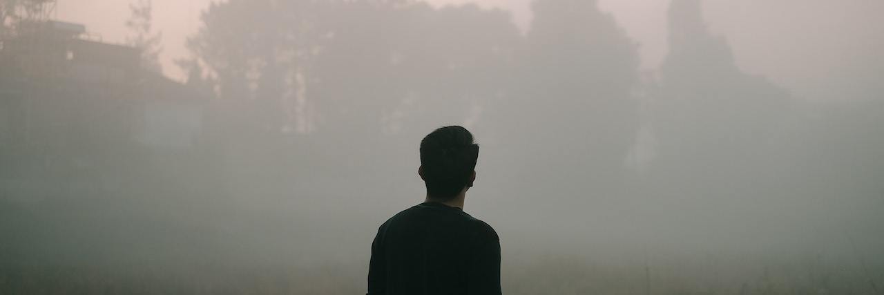 A man wearing dark clothes, standing outside in fog