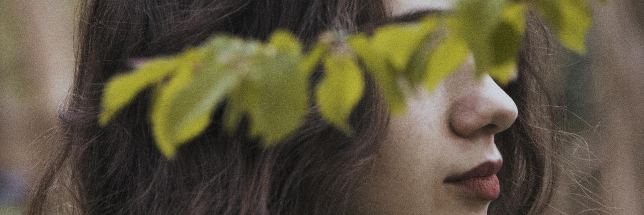 photo of a woman with dark hair and eyes hidden by leaves