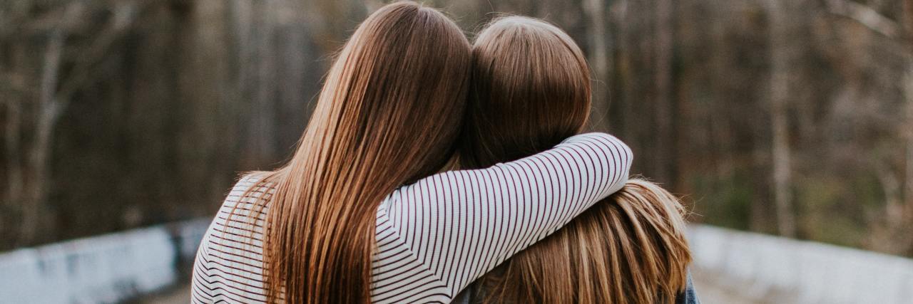Why Validation Is Important in Supporting Trauma Survivors photo of two women, one with her arm around another, standing on road with trees and facing away from camera