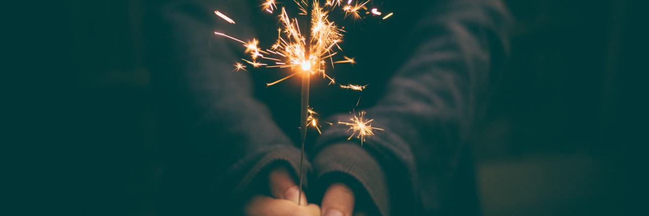 close up photo of woman holding a sparkler in almost darkness