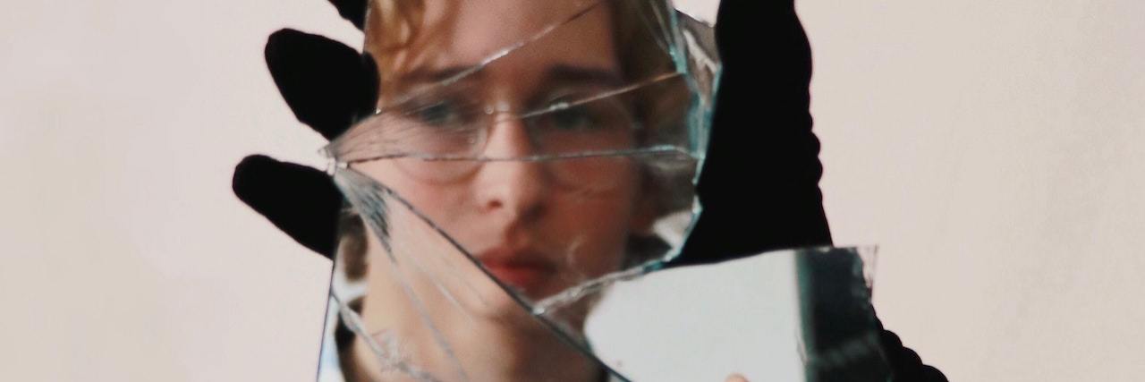 A broken mirror reflecting the image of a blonde woman with glasses