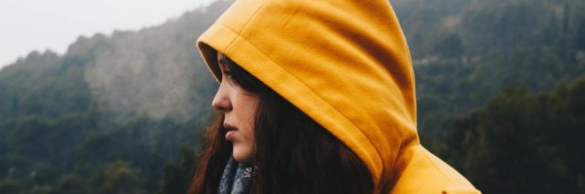 photo of woman wearing a yellow raincoat in profile view with foggy mountains behind her