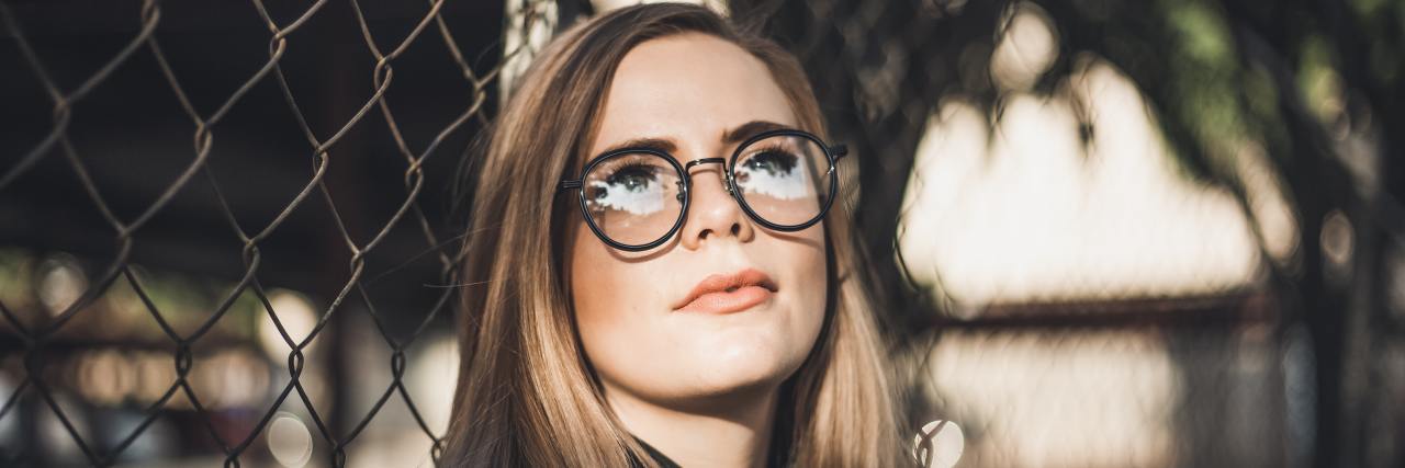 My Antipsychotic Stopped My Hallucinations, but Now I Fear Silence girl with long hair in glasses, standing against a fence looking out into the distance
