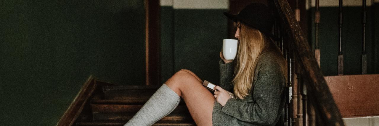 What I Wish I Knew About Life With Bipolar Disorder As a Teen photo of young woman sitting on stairs drinking tea with a book in her lap