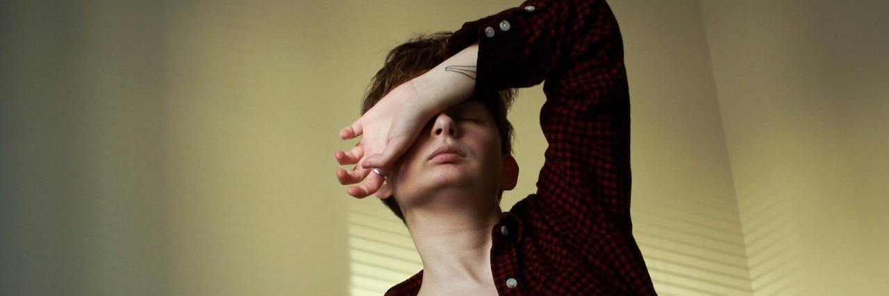 A woman with short hair wearing a flannel, covering her face with her hand