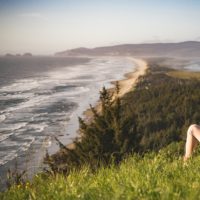 Photo of a white woman in a flannel shirt sitting on a hill overlooking water