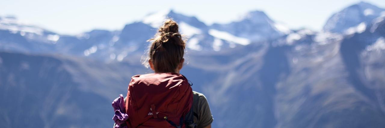 Backpacking Alone Is My Self-Care Image of woman wearing a backpack looking out over mountains