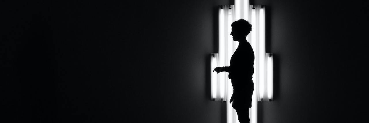 Profile of a person standing in a dark room backlit by light from a narrow window