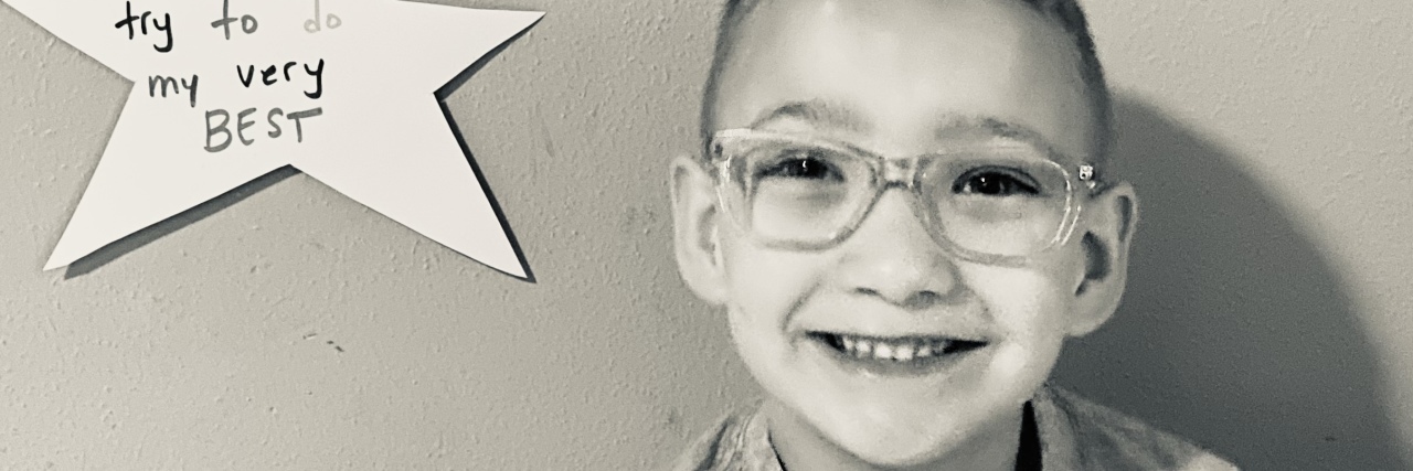 The Truth Behind 'I’m Fine' as the Parent of a Child With a Disability Stephanie's son next to a paper star award he earned on the wall.