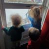 three young children looking out a window
