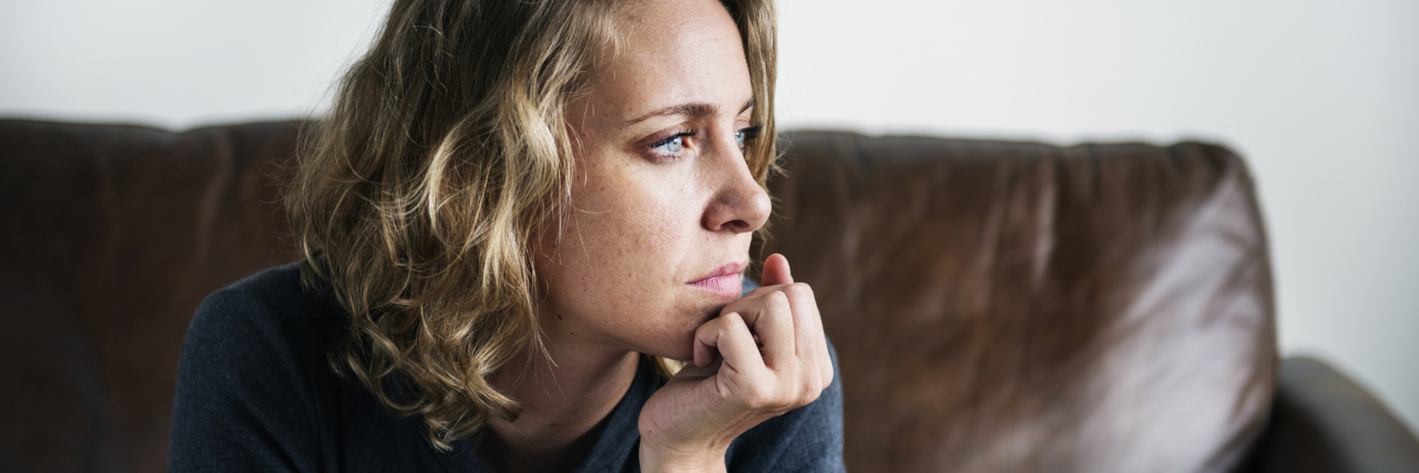 photo of woman sitting on couch, looking worried and looking out of unseen window