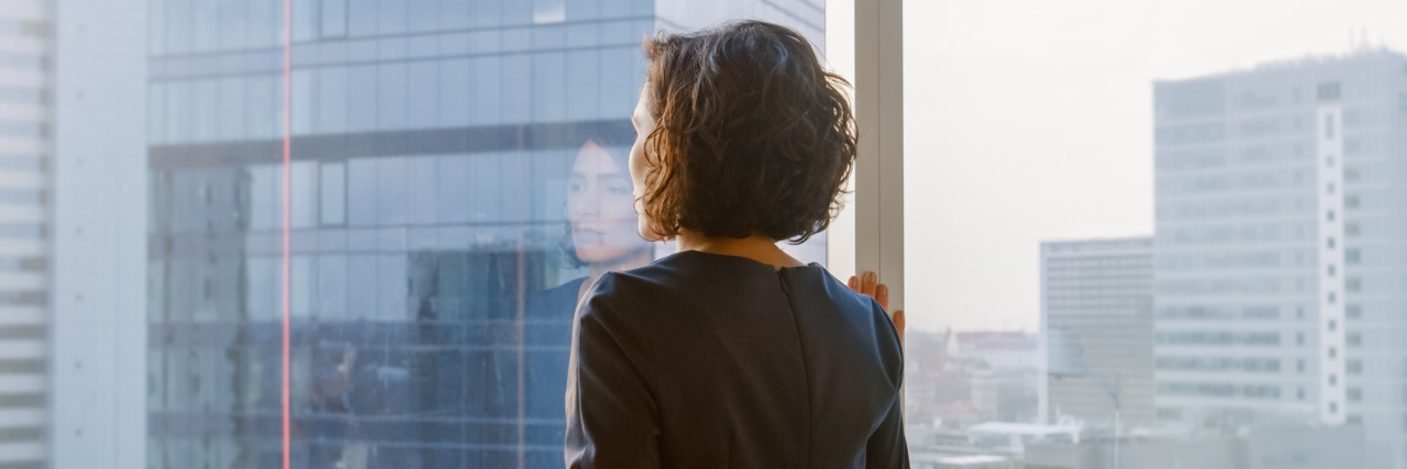 The Impact COVID-19 Has Had on Me as a Mental Health Professional back of a woman looking out a glass window in a city thoughtfully