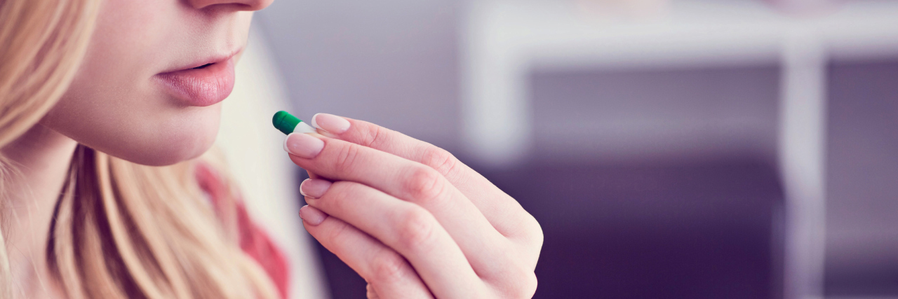 Taking Psychiatric Medication Can Be a Form of Mental Health Self-Care photo of young woman taking pill, raising it to her mouth while holding a glass of water