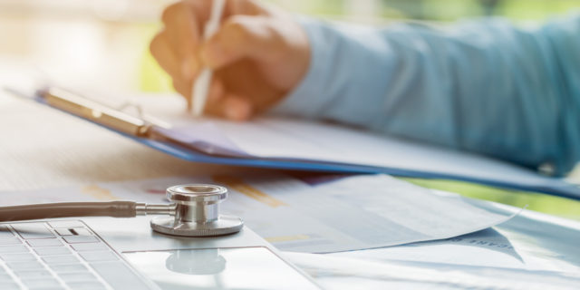 Doctor working in hospital writing on prescription clipboard.