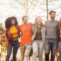 group of multiracial young adults with arms around each other smiling