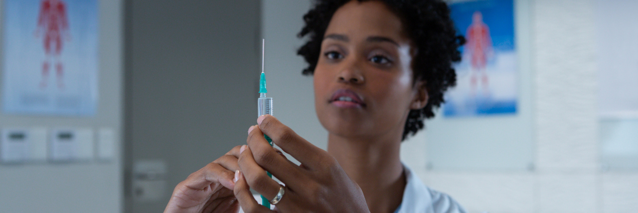 As COVID-19 Vaccine Rollout Expands, Black Americans Still Left Behind female doctor holding syringe with injection in the hospital.