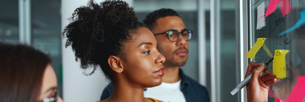 How Employers and Managers Can Support Employee Mental Health Black businesswoman and Black businessman writing on adhesive notes stuck over glass