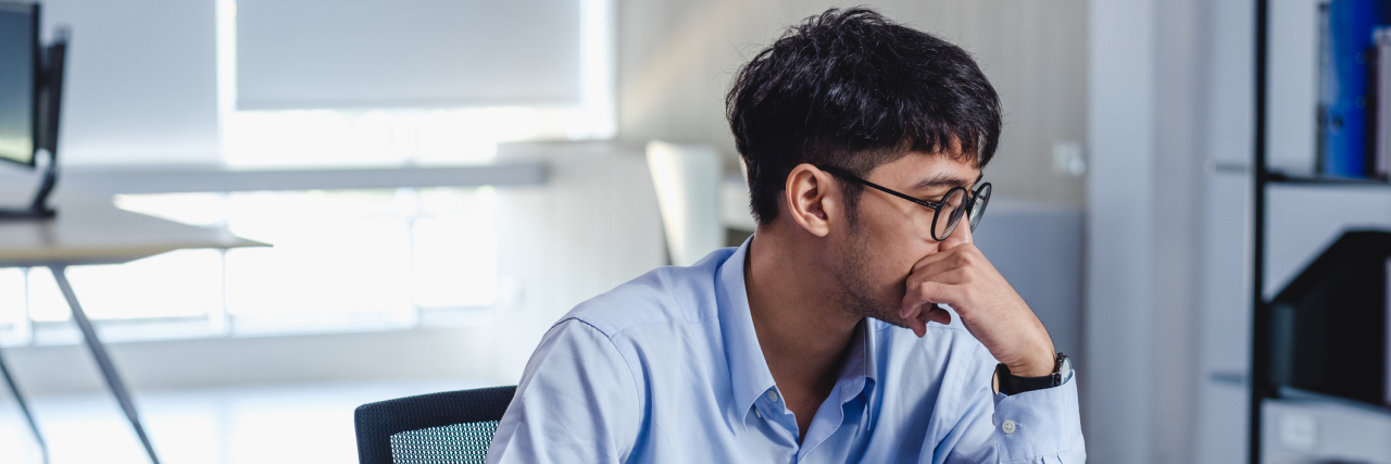 Study Suggests Small Slights at Work Can Lead to Suicidal Thoughts Man in front of his open laptop wearing a blue-collared shirt and glasses, looking away distressed