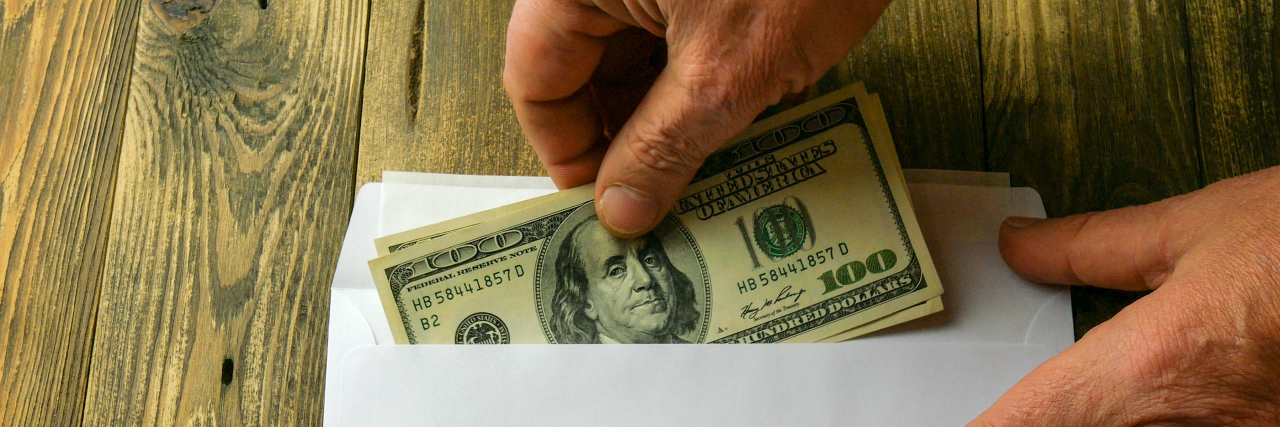 Why Excluding Adult Dependents From COVID-19 Relief Plans is Ableist Someone's hand puts hundred dollar bills in an unsigned envelope