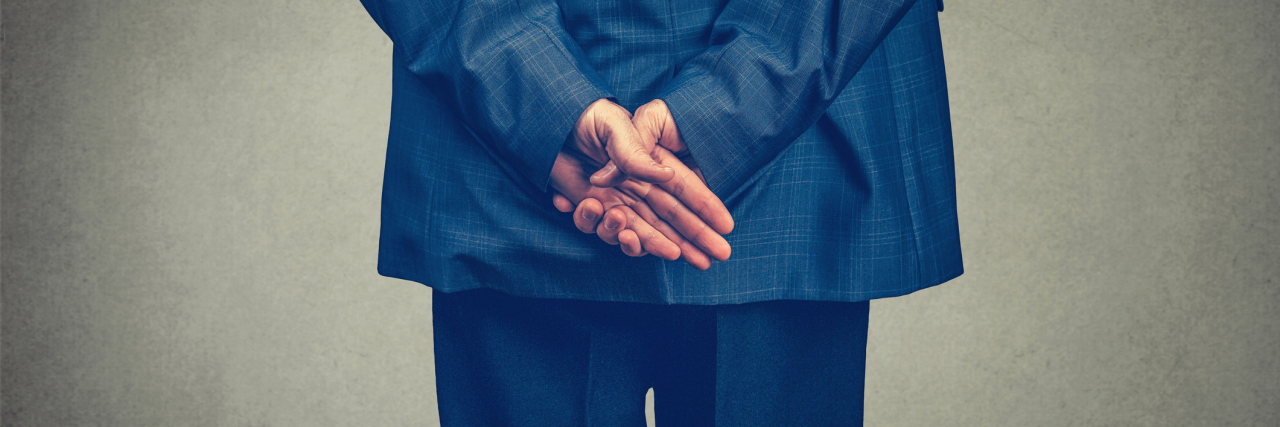 Back of a man's dark blue suit, hands behind his back