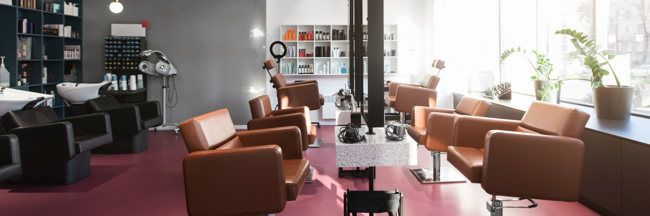 Working at a Salon Taught Me We Need More Mental Health Resources Inside of a beauty salon, a pink floor lined with styling stations and leather chairs