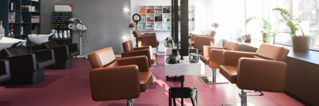 Inside of a beauty salon, a pink floor lined with styling stations and leather chairs