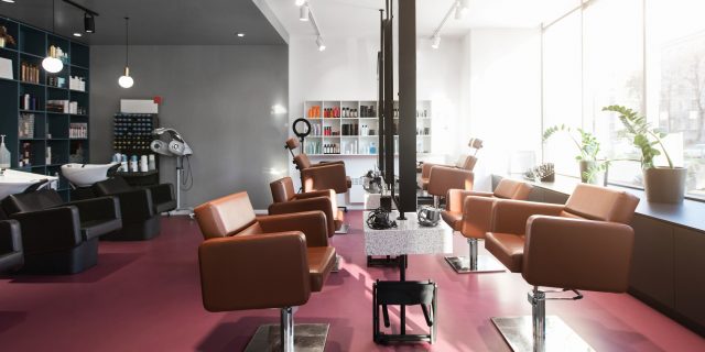 Inside of a beauty salon, a pink floor lined with styling stations and leather chairs