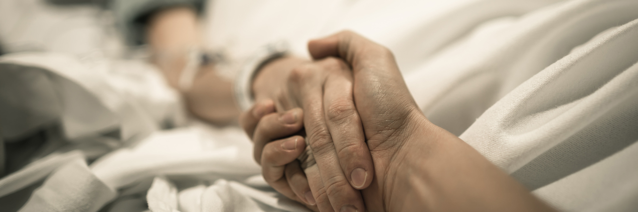 To the Healthcare Professionals Who Go the Extra Mile for Patients Woman lying in hospital bed with hand being held.