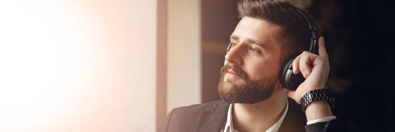 How Making Playlists for My Kids Helps Me Cope With Suicidal Thoughts A white man in a suit sitting at a cafe with headphones, looking out the window