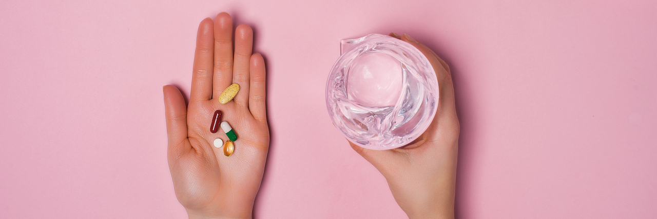 woman's hand with different colored pills in one and a glass of water in another