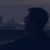 photo of young man sitting beside window at dusk, looking over city