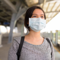 Young Filipino woman wearing a blue surgical mask at a train station, looking out at the sky