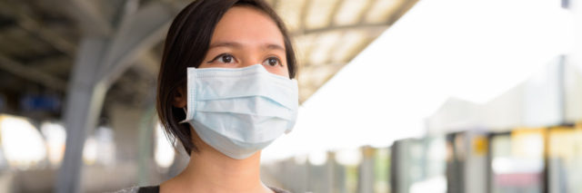 Young Filipino woman wearing a blue surgical mask at a train station, looking out at the sky