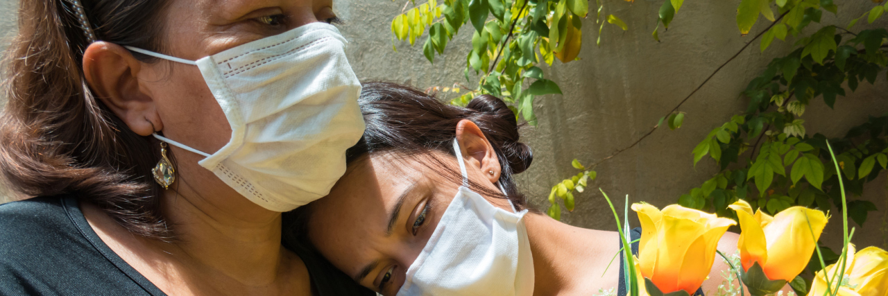 'Last Responders' Brace for Surge in COVID Deaths Across US Mother and daughter, both wearing facemasks mourn the loss of COVID-19 patient with yellow roses