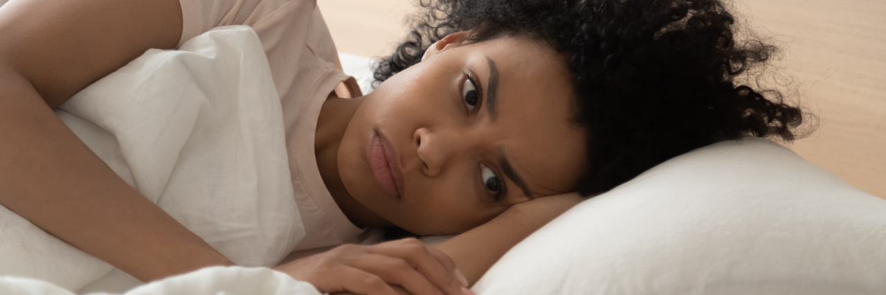 The Physical Effects of Anxiety on My Body Sleepless looking woman lying with her head ona. pillow, hand under her head, eyes open and staring away