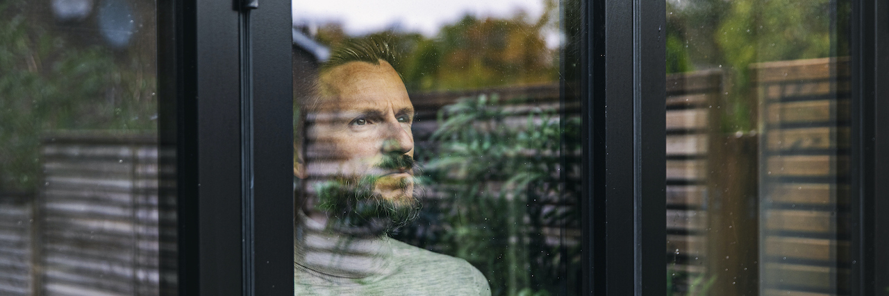 Man looking through window with outside greenery reflected on it