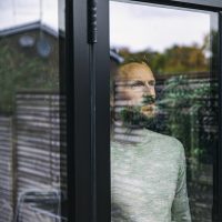 Man looking through window with outside greenery reflected on it