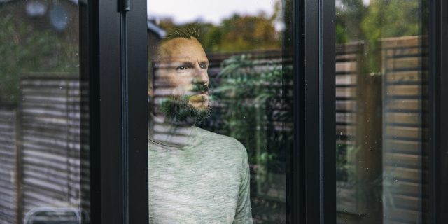 Man looking through window with outside greenery reflected on it