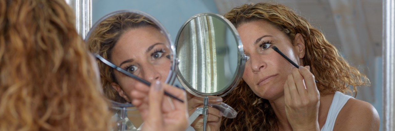a woman applying her makeup in a mirror