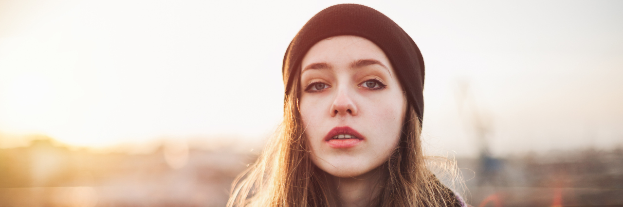 portrait of a young, white woman in a red beanie with long, brown hair looking at the camera with a straight face