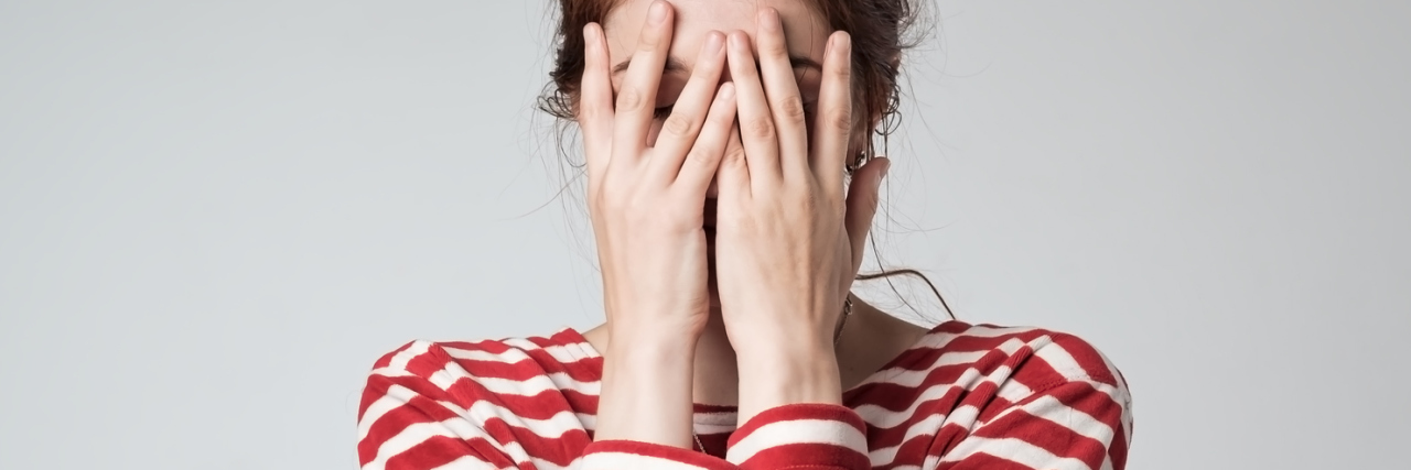 When People Think You're 'Put Together' Despite Depression Photo of young woman in striped t-shirt covering her face with her hands