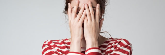 Photo of young woman in striped t-shirt covering her face with her hands