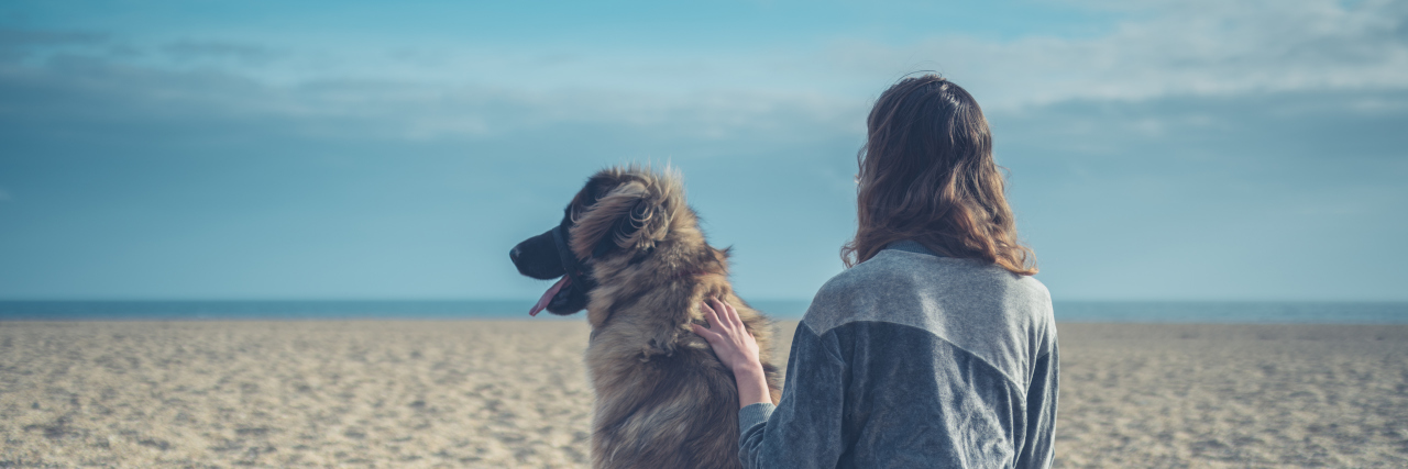 What It’s Like to Date When You Have a Service Dog Young woman sitting on beach with big dog.