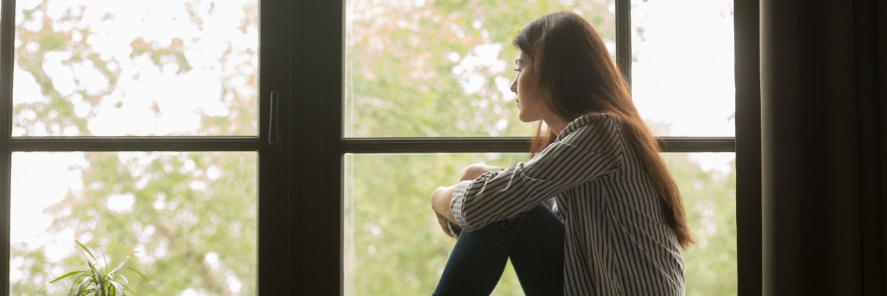 When You're Feeding an Intrusive Thought Without Realizing It photo of young woman sitting by window looking out, knees raised