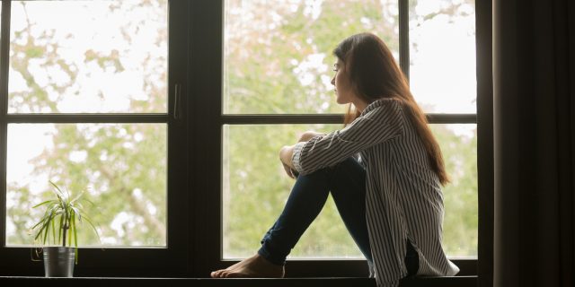 Teen With Epilepsy Calls Out Company After Being Judged for Using Disability Seating photo of young woman sitting by window looking out, knees raised
